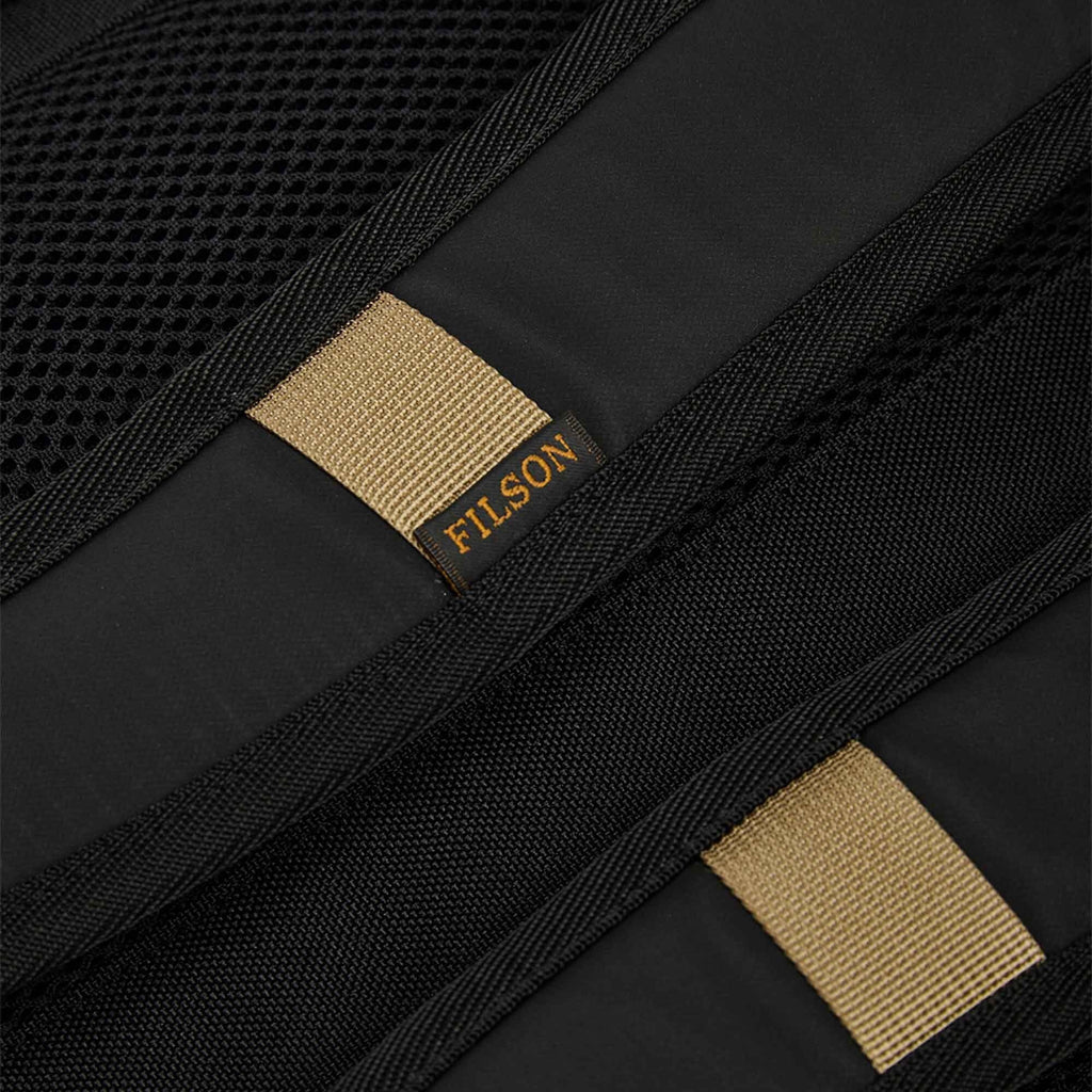 Scout Journey backpack strap close-up with tan label tab and FILSON branding.