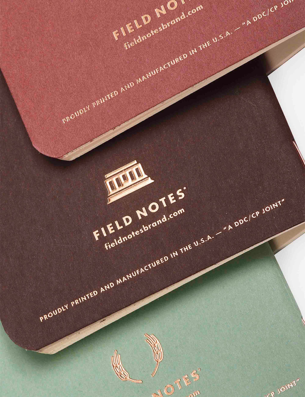 Three stacked quarterly memo books showing bottoms in maroon, dark brown, and mint