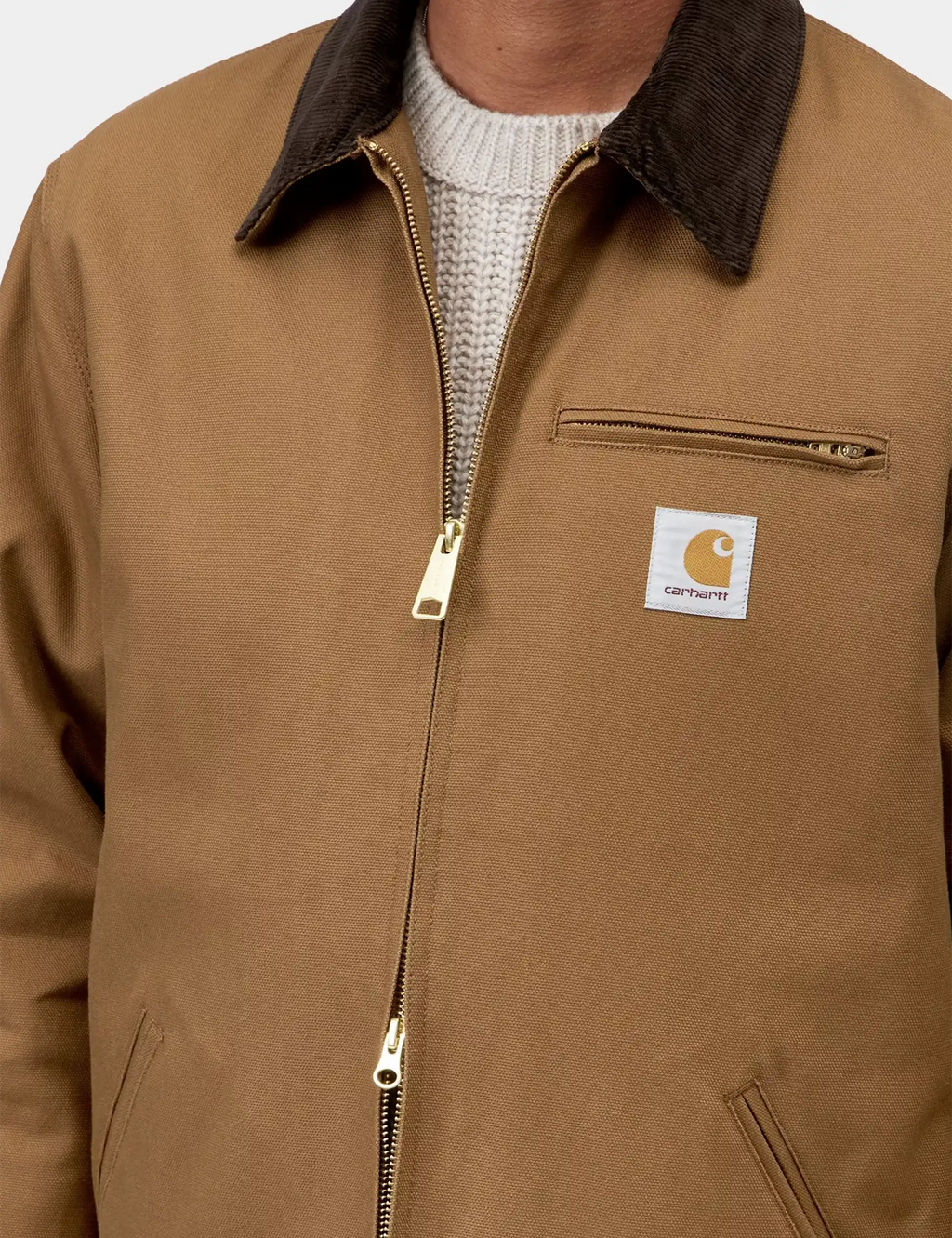 Tan jacket chest pocket with zipper and Carhartt logo patch, dark collar