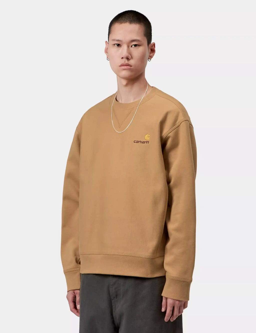Carhartt WIP crew sweatshirt in dusty tan with chest script logo, worn over dark pants