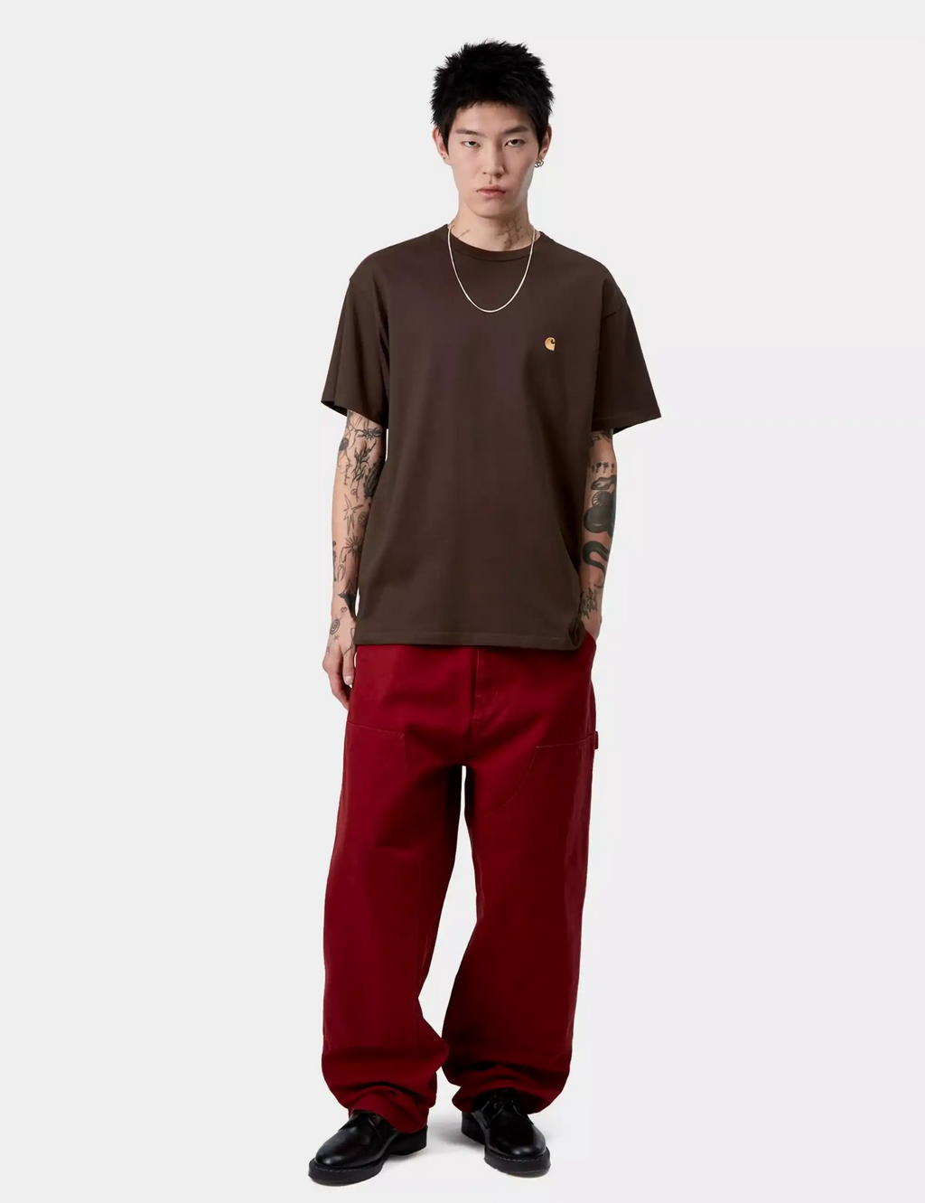 Brown crew-neck T-shirt with gold chest logo, worn with red pants.