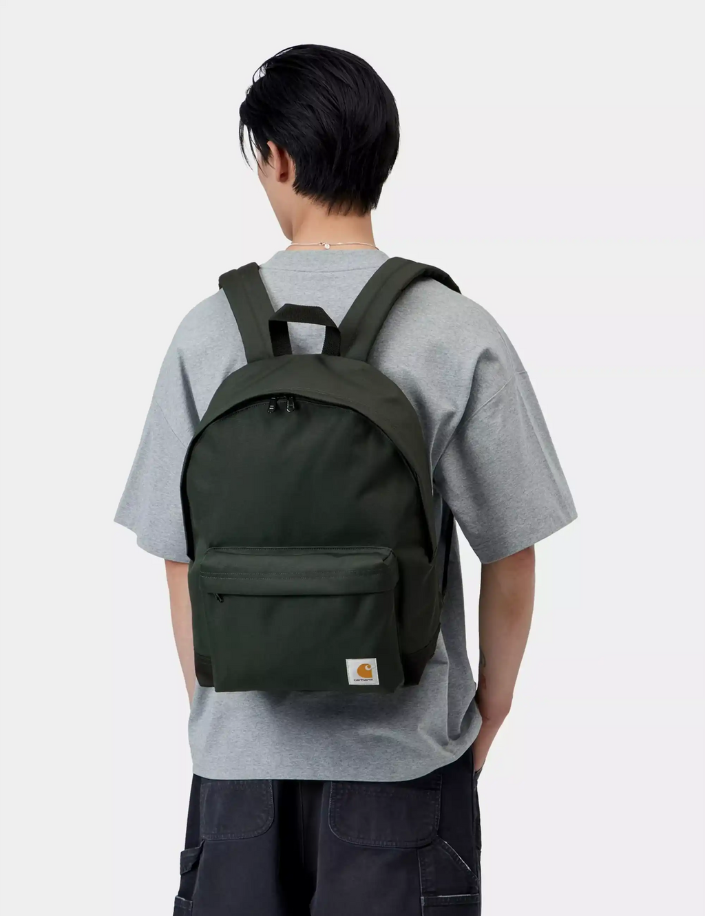 Dark green backpack with front zip pocket and top handle, worn on back