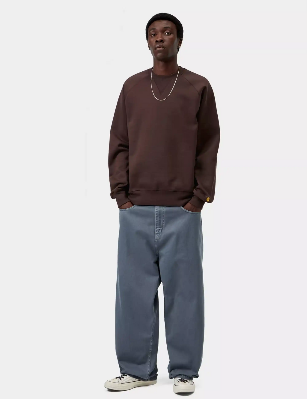 Brown crewneck sweatshirt with gold cuff logo worn with light blue jeans