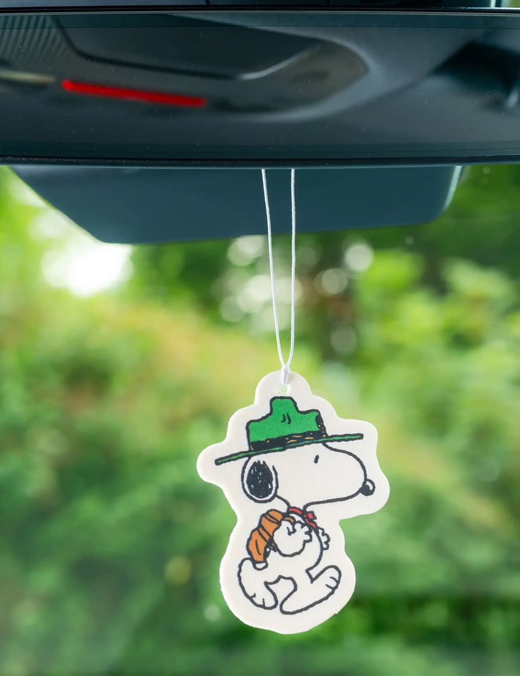 Snoopy air freshener charm hanging from a car mirror