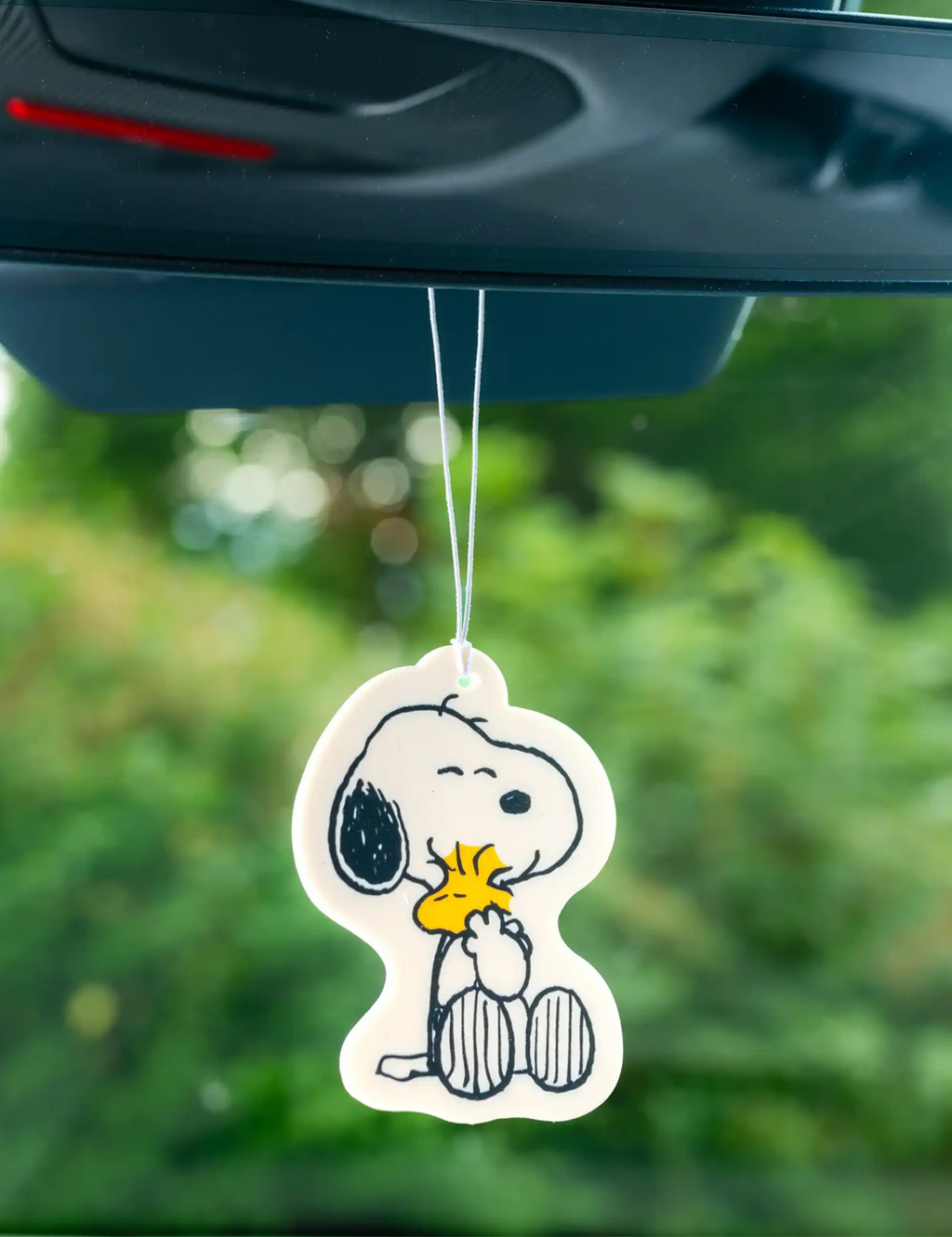 Peanuts air refreshener tag with Snoopy holding a small pup, hanging from cord