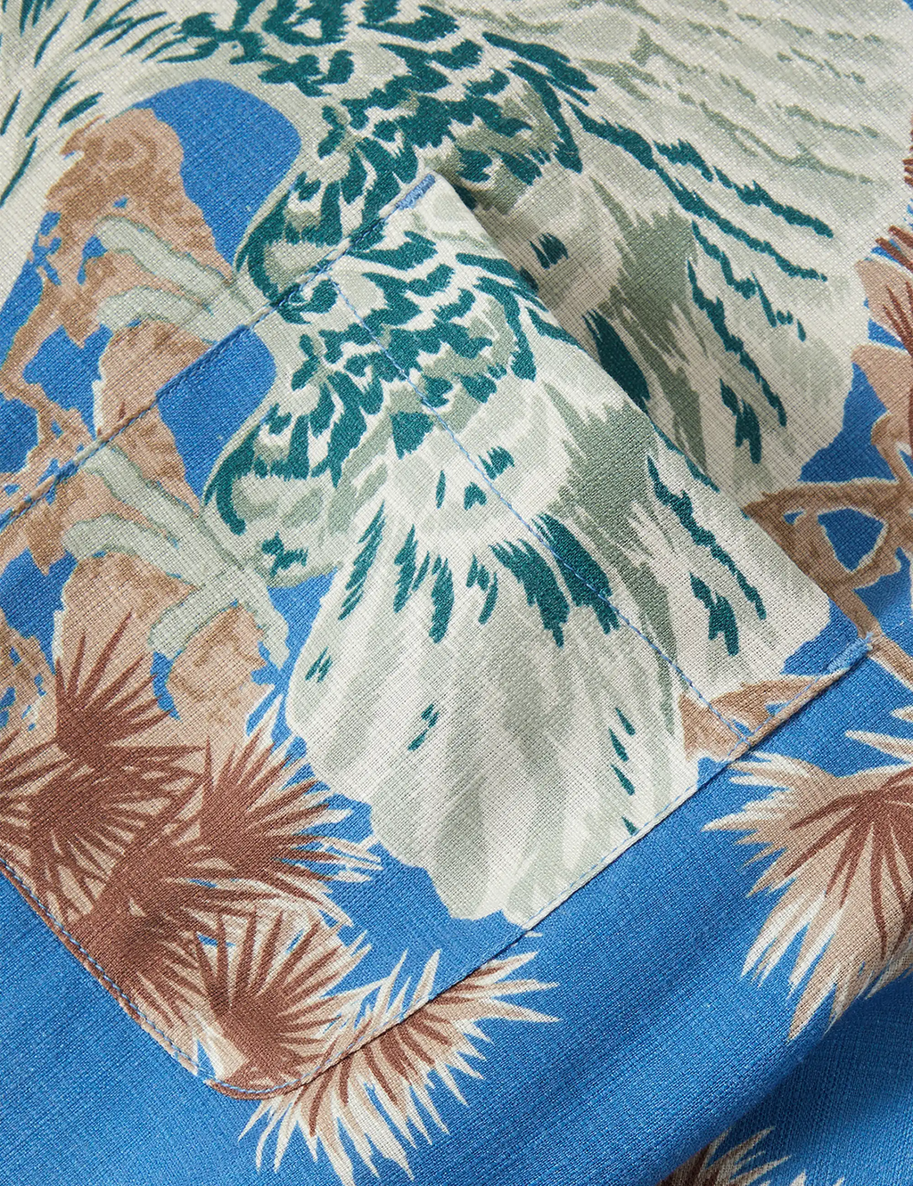 Blue woven Hawaiian shirt fabric close-up with tropical leaf and palm print