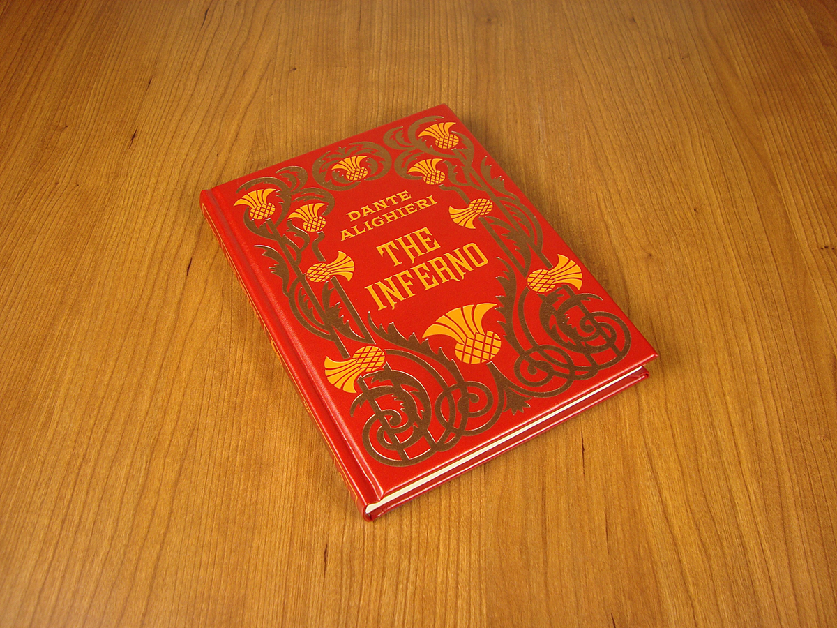 Red hardback book with gold “THE INFERNO” title, lying on wooden tabletop