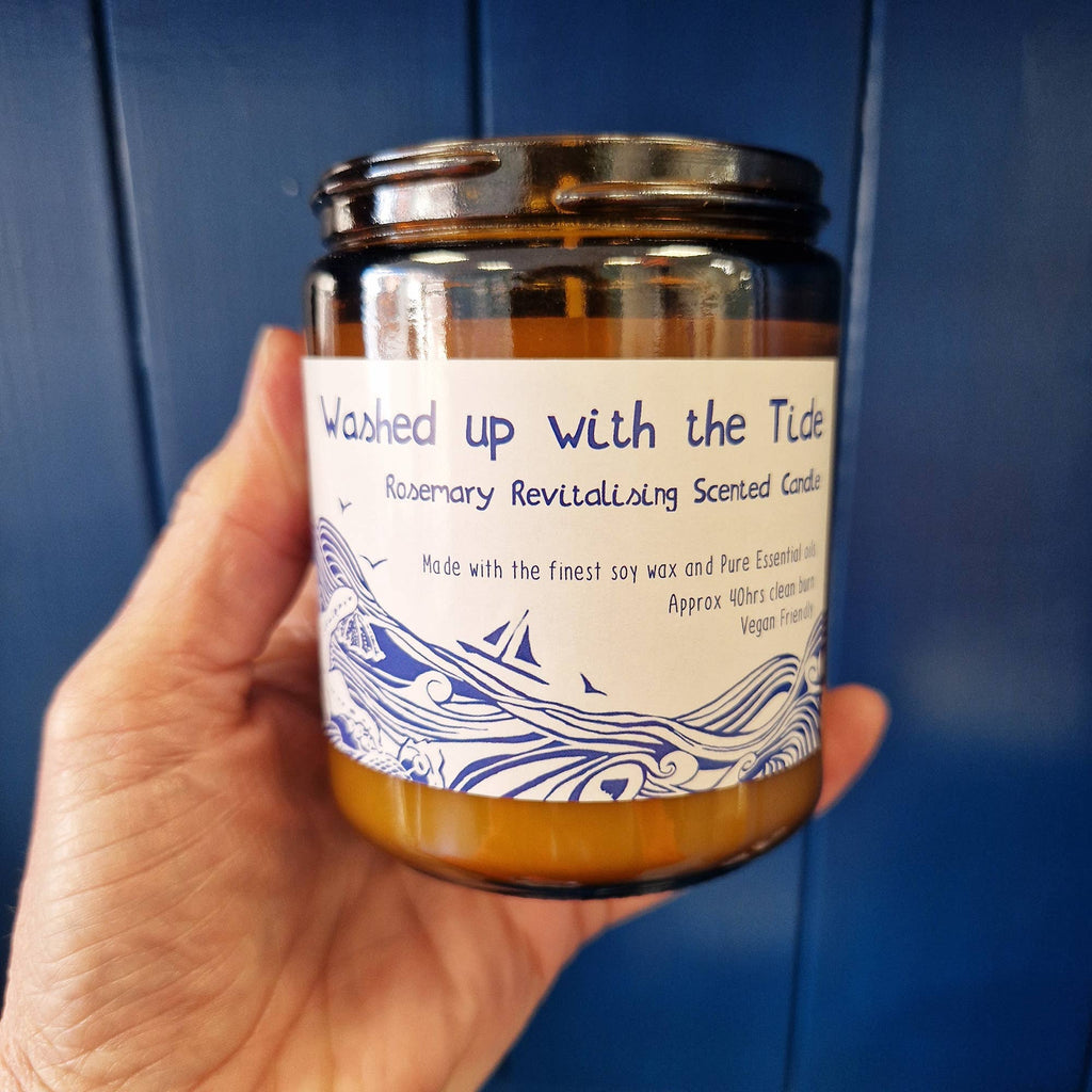 Hand holding an amber candle jar with white lid and blue label