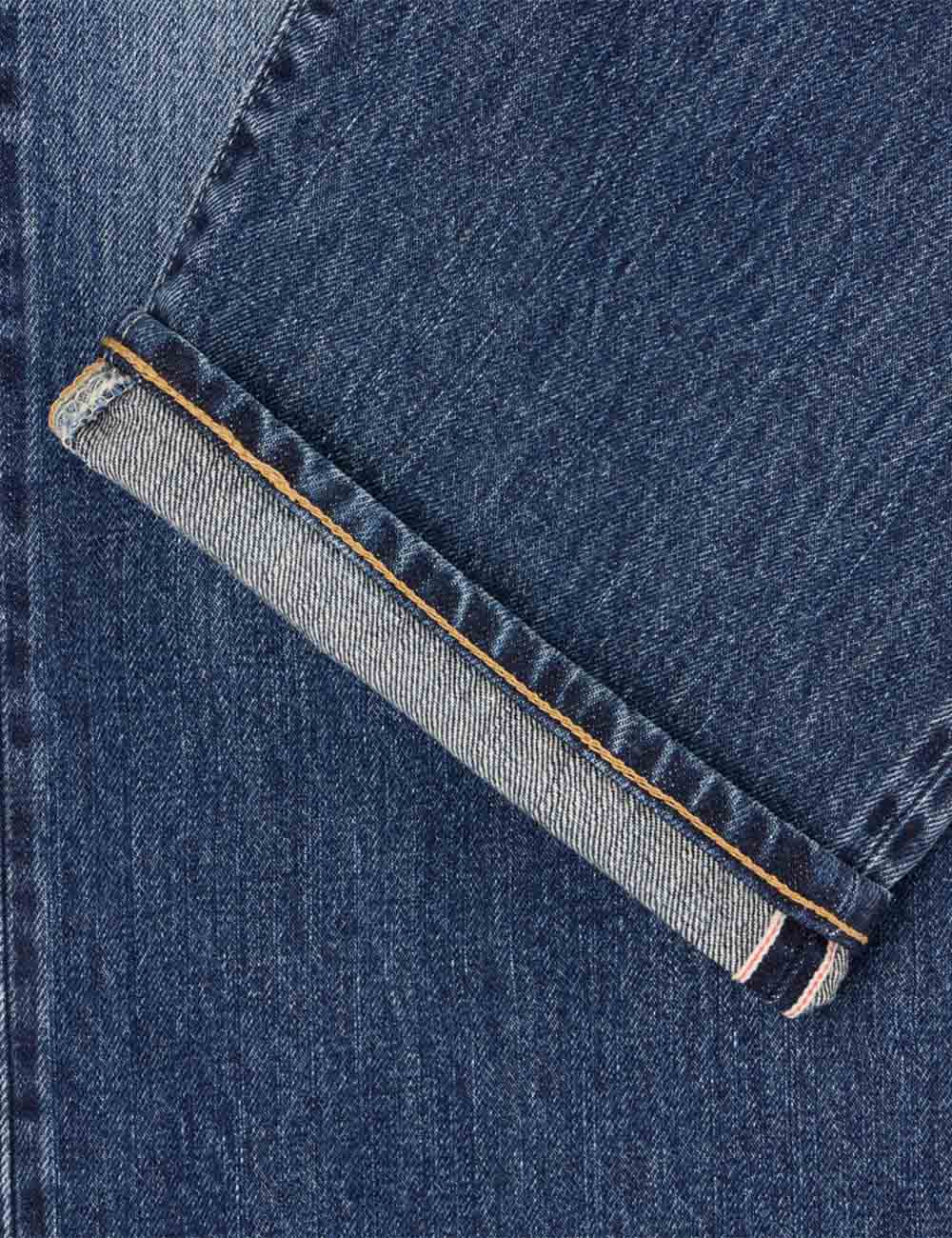 Dark blue denim jeans close-up, visible selvedge edge with orange-brown trim