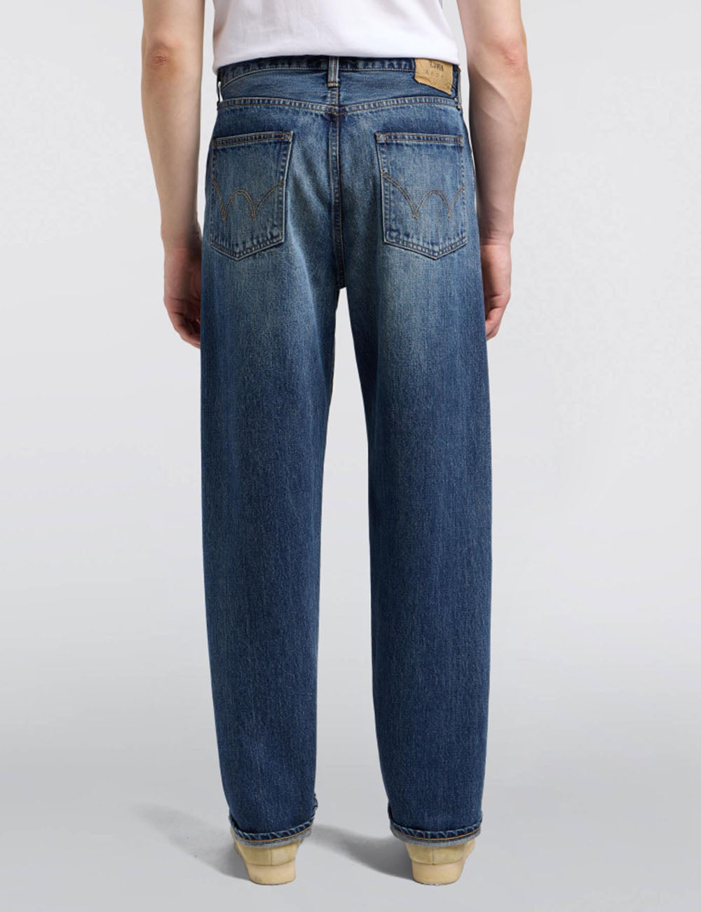 Loose dark blue denim jeans, back view with two button-flap pockets and belt loops