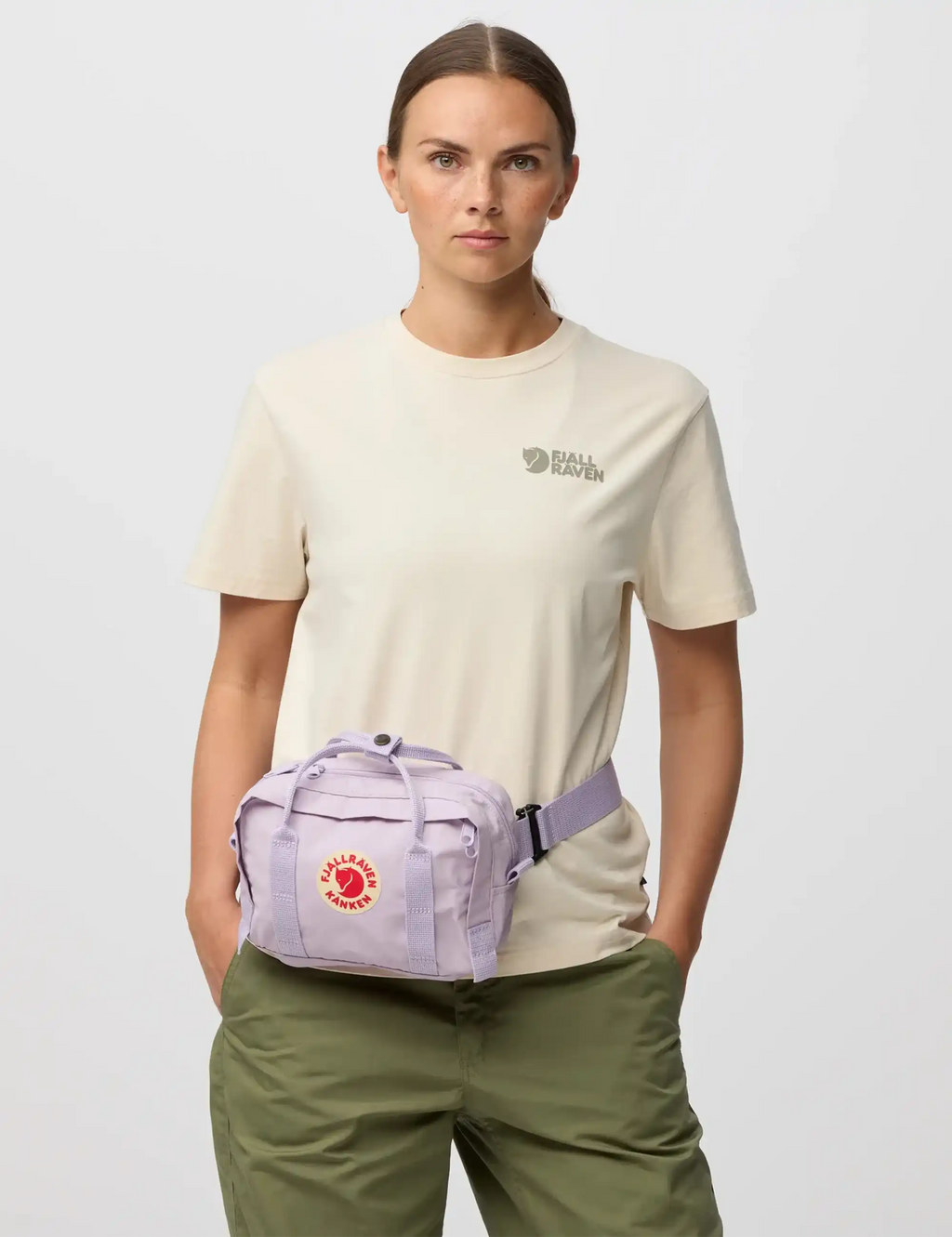 Pastel lavender crossbody bag worn crossbody with red logo patch and front pocket