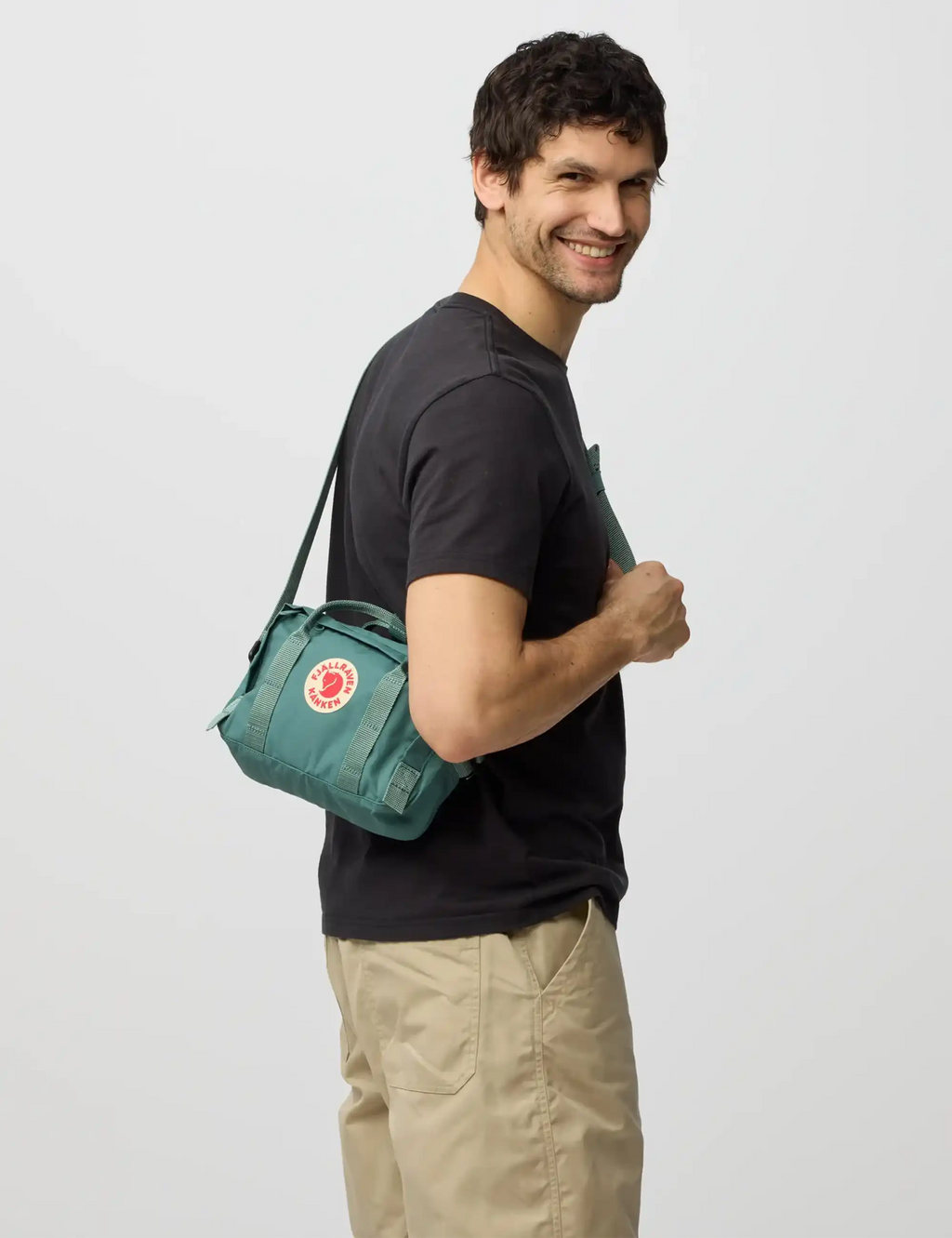 Frost green crossbody bag worn on front, red logo patch and adjustable strap.