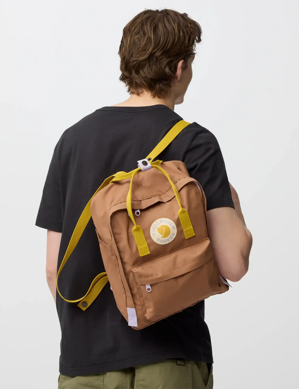 Khaki backpack worn from behind with yellow straps and circular logo patch