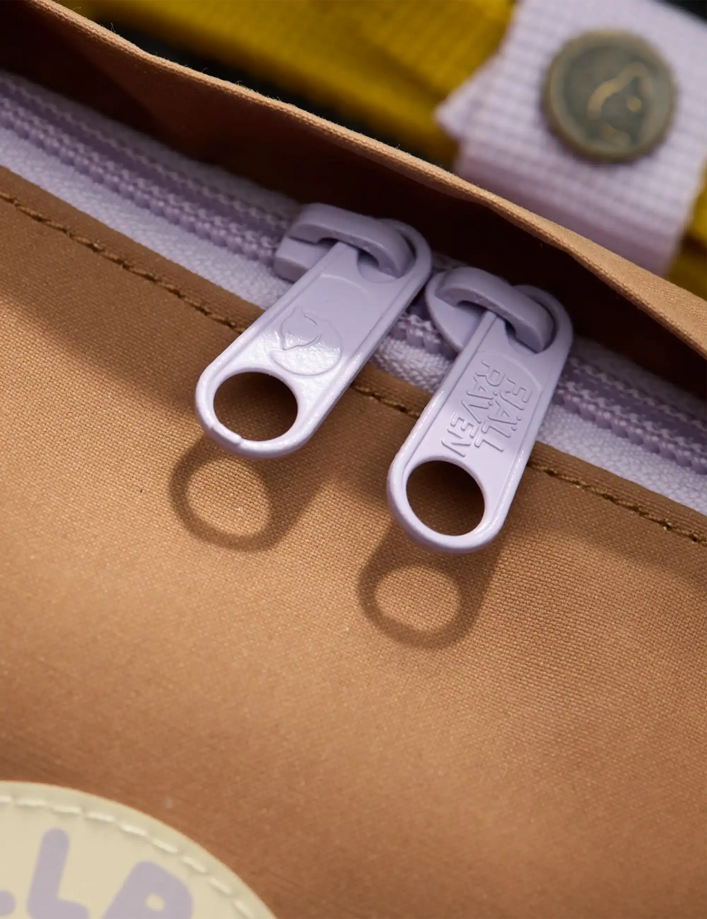 Khaki backpack zipper tabs and fabric trim near pocket opening