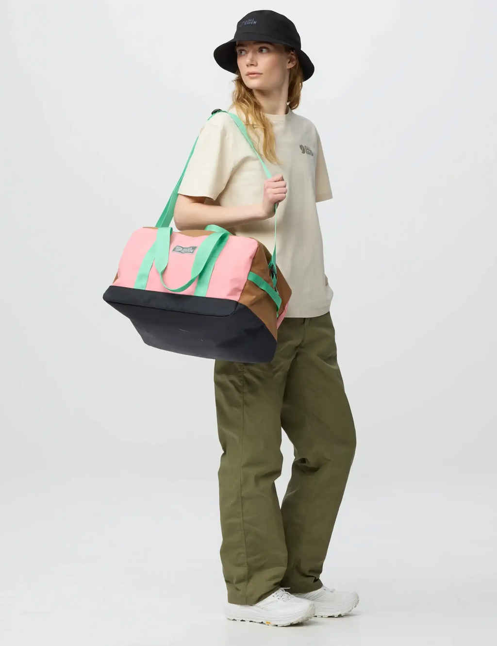 Fjäll Räven duffel bag held crossbody, pink with green straps and black base