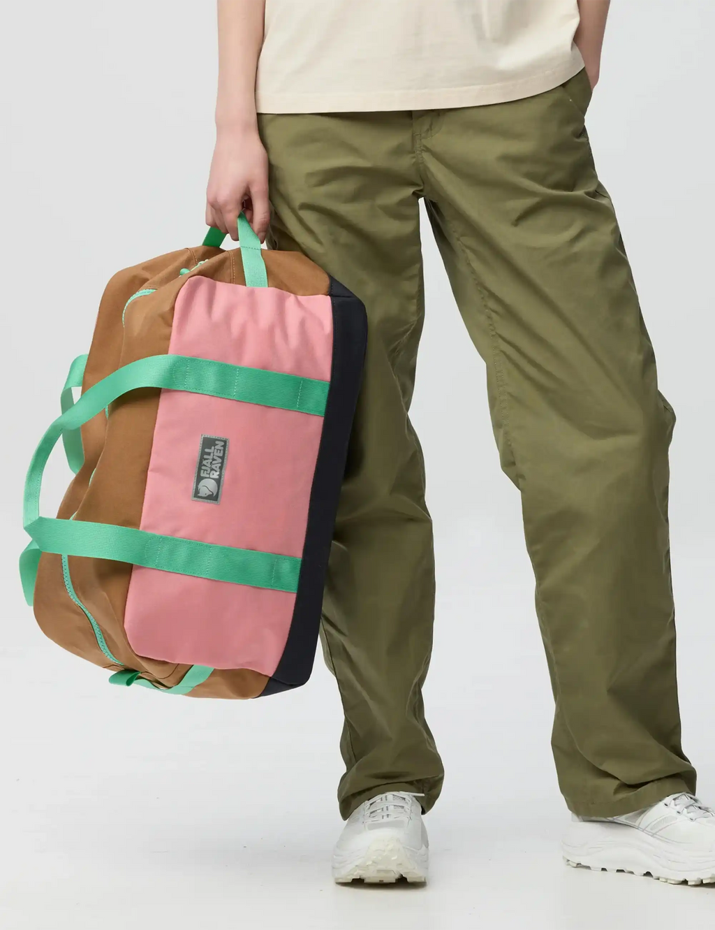 Fjäll Räven duffel bag held close, pink body with green straps and black base